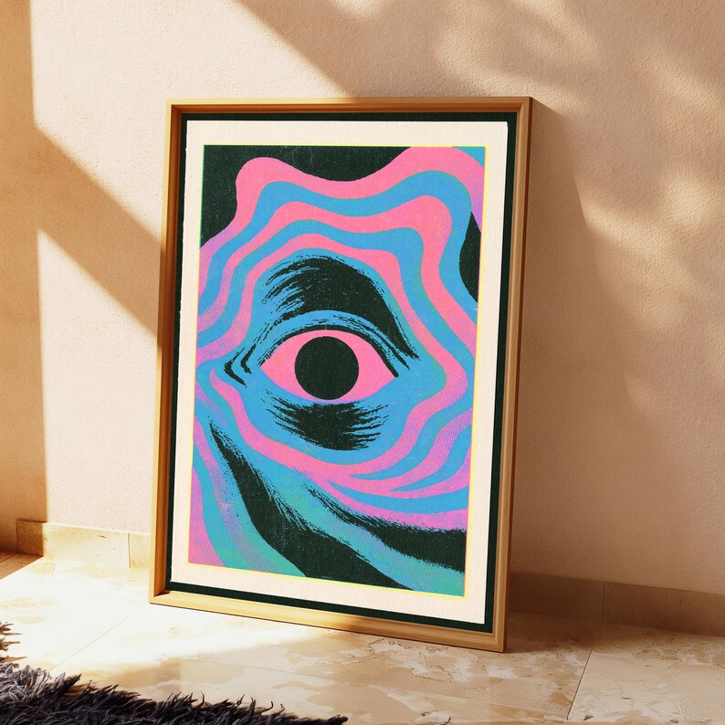 May include: A framed rectangular art print featuring a central human eye surrounded by concentric, wavy bands of bright pink and cyan blue. The eye has a solid black pupil and dark, textured shading, set against a deep black background.