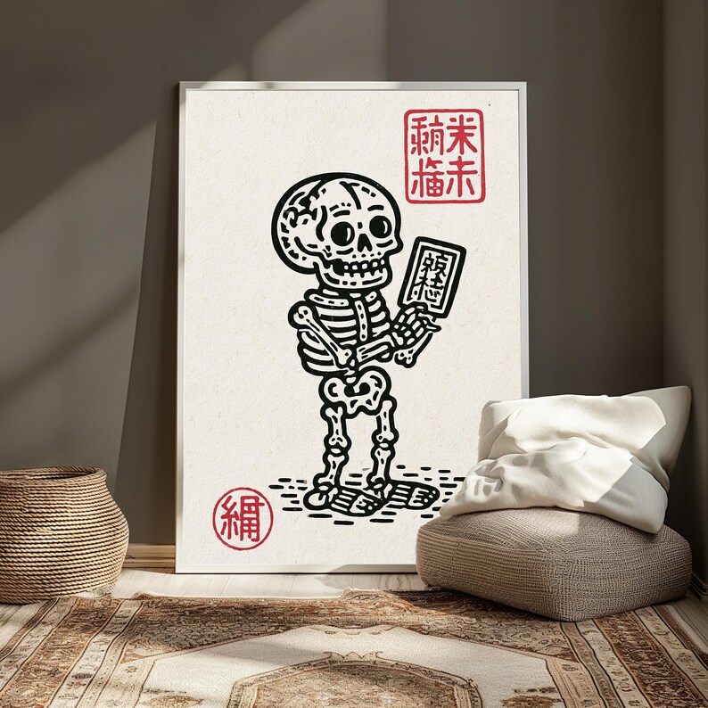 May include: A framed wall art print featuring a black ink illustration of a skeleton holding a small rectangular tablet. The design includes red stamp-like symbols with East Asian characters in the top right and bottom left corners on a cream background.