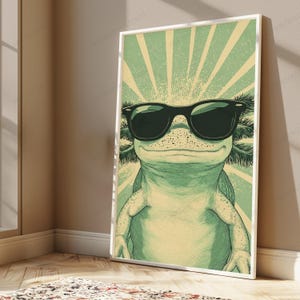 May include: A framed vertical wall art print featuring a stylized illustration of an axolotl wearing black sunglasses. The axolotl is light green with darker green feathery gills and a background of radiating light green and cream sunburst lines.
