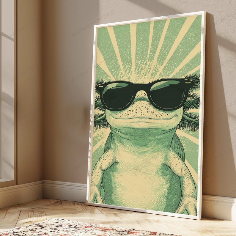May include: A framed vertical wall art print featuring a stylized illustration of an axolotl wearing black sunglasses. The axolotl is light green with darker green feathery gills and a background of radiating light green and cream sunburst lines.