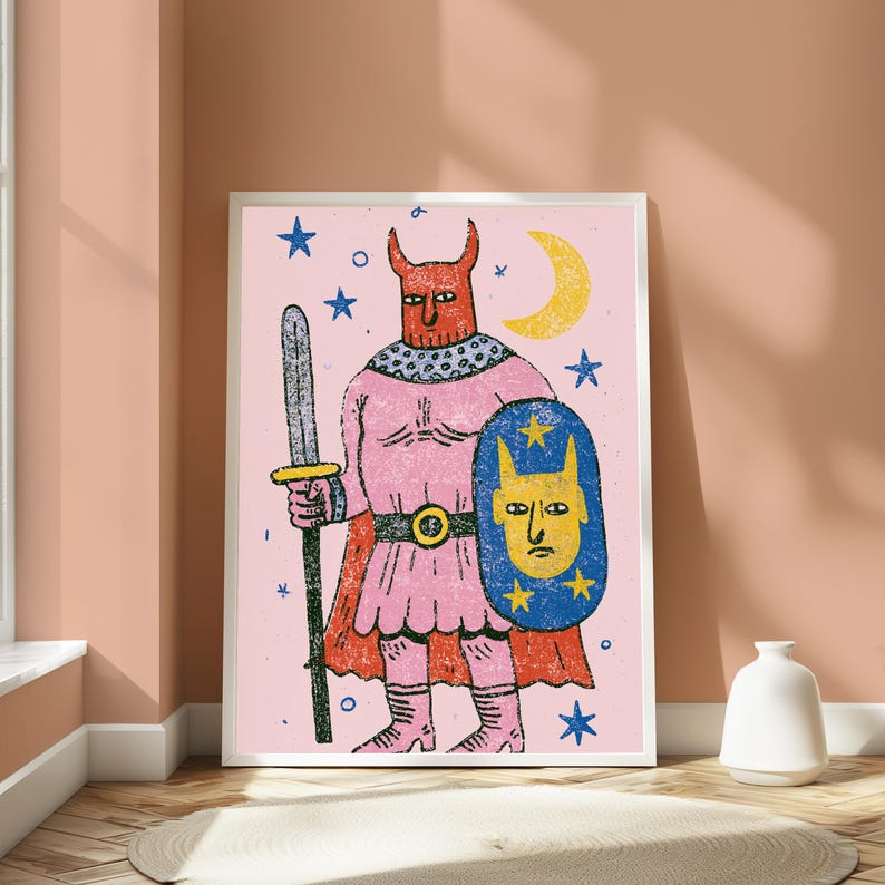 K&ouml;nnte beinhalten: Ein gerahmter Kunstdruck auf hellrosa Hintergrund zeigt eine geh&ouml;rnte Figur in einer rosa Tunika und einem roten Umhang. Die Figur h&auml;lt ein graues Schwert und einen blauen Schild mit einem gelben Gesicht und Sternen. Ein gelber Halbmond und blaue Sterne umgeben die Figur.