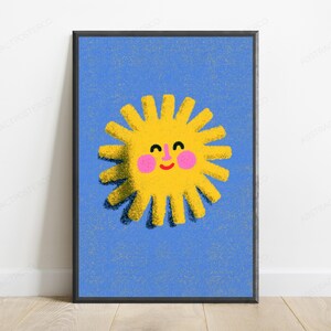 May include: A framed wall art print featuring a bright yellow sun with a smiling face, pink cheeks, and a red mouth, centred on a textured blue background. The sun has numerous rays extending outward, creating a cheerful and simple graphic illustration.