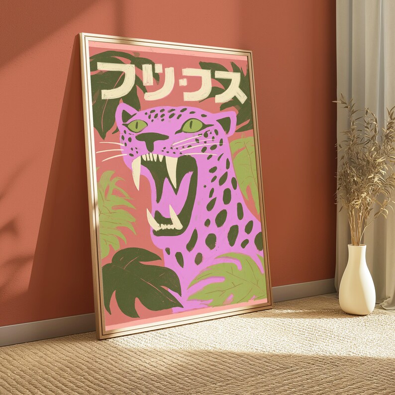 May include: A framed wall art print featuring a stylized pink leopard with dark spots and green eyes, shown with its mouth open to reveal sharp teeth. The background includes green tropical leaves and Japanese text in cream-colored lettering.