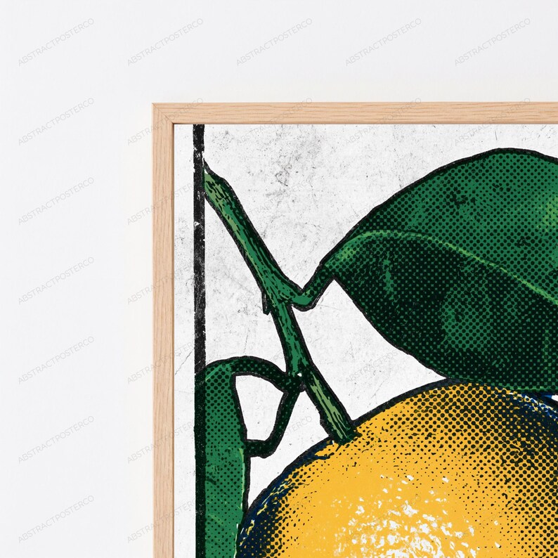 May include: A framed wall art print featuring a pop art style illustration of a yellow citrus fruit with green leaves. The design uses a halftone dot pattern on a textured white background, enclosed within a light-colored wooden frame.