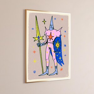May include: A framed wall art print featuring a stylised illustration of a figure in a pink suit with a pointed hood, holding a long yellow spear with an eye motif and a blue shield with a star, set against a light brown background with stars.