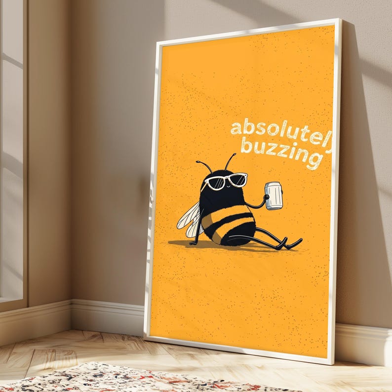 May include: A framed rectangular wall art print featuring a yellow background with a black and yellow bee wearing white sunglasses, sitting and holding a silver can. The text "absolutely buzzing" is printed in white in the upper right corner.