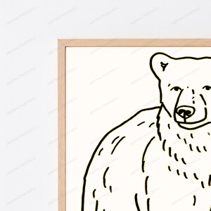K&ouml;nnte beinhalten: Ein gerahmter Wandkunstdruck mit einer schwarzen Strichzeichnung eines B&auml;ren auf wei&szlig;em Hintergrund. Der B&auml;r ist von der Brust aufw&auml;rts dargestellt und zeigt Kopf und Schultern mit einfachen, klaren Strichen. Der Rahmen besteht aus hellem Holz.