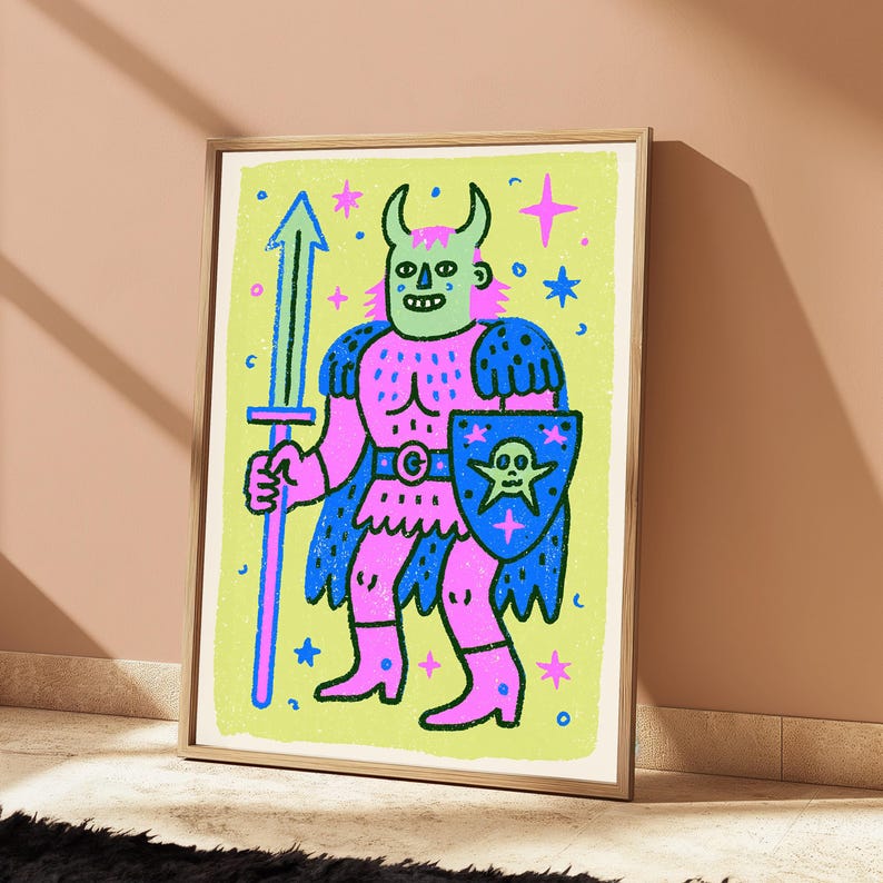 May include: A framed art print featuring a stylized illustration of a horned warrior figure in pink and blue armor. The figure holds a long sword and a shield with a skull emblem. The background is light green with scattered pink and blue stars.
