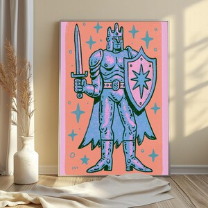 May include: A framed art print featuring a stylized illustration of a knight in armor holding a sword and a shield with a star emblem. The knight is rendered in shades of blue and pink against a coral background, surrounded by small blue stars.