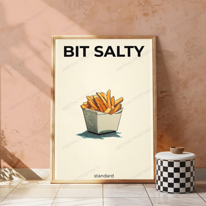 May include: A framed vertical poster featuring a cream-colored background with the bold black text BIT SALTY at the top. Centered below is a hand-drawn illustration of golden-brown french fries in a white container, with the word standard below.