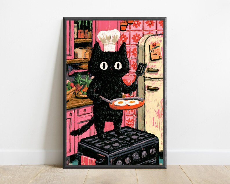 Peut inclure: Une impression d'art encadr&eacute;e repr&eacute;sentant un chat noir portant une toque de chef blanche, debout sur une cuisini&egrave;re noire dans une cuisine rose. Le chat tient une spatule et une po&ecirc;le contenant deux &oelig;ufs au plat. Fond avec placards roses.
