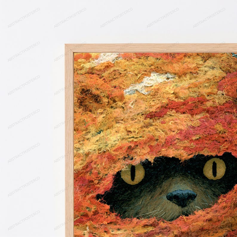 May include: A framed wall art print featuring a close-up of a dark-furred animal with bright yellow eyes peeking out from beneath a thick, textured layer of vibrant orange, red, and yellow fibres that resemble autumn leaves or fur.