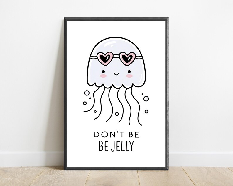 May include: A framed wall art print featuring a white cartoon jellyfish with pink cheeks and heart-shaped sunglasses. The jellyfish has long wavy tentacles and small bubbles around it. Below the illustration, the text reads DON'T BE BE JELLY.