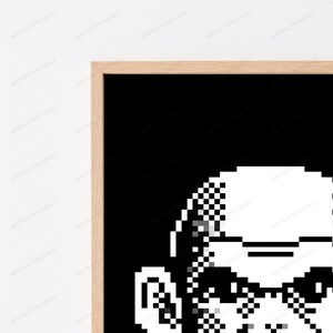 May include: A framed wall art print featuring a high-contrast, black and white pixel art graphic. The design displays a stylized, blocky character portrait composed of square pixels against a solid black background, encased in a light wood frame.