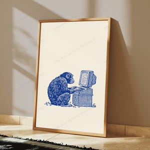 May include: A framed vertical wall art print featuring a blue line-art illustration of a chimpanzee sitting at a desk and typing on a vintage computer. The background of the print is a solid cream color, and the frame is a thin metallic gold.