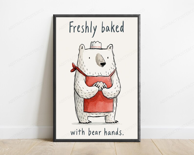 Puede incluir: Una l&aacute;mina enmarcada que muestra un oso blanco con un delantal rojo y un peque&ntilde;o gorro de chef blanco. El oso est&aacute; sobre un fondo crema con el texto "Freshly baked" en la parte superior y "with bear hands." en la parte inferior en negro.