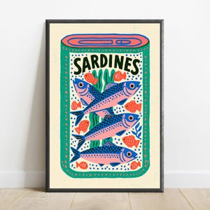May include: A rectangular art print featuring a stylized illustration of an open tin of sardines. The design includes three large blue and pink fish, several smaller orange fish, and green seaweed accents on a cream background with the text SARDINES.