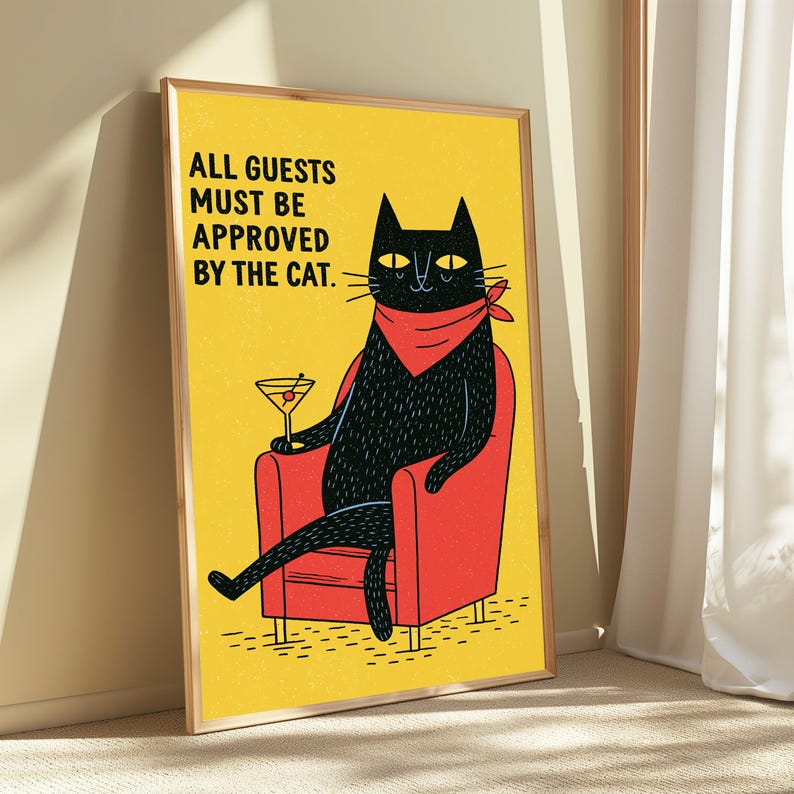 May include: A framed wall art print featuring a black cat wearing a red bandana, sitting in a red armchair while holding a martini glass. The background is yellow with the black text: ALL GUESTS MUST BE APPROVED BY THE CAT. The print is in a wooden frame.