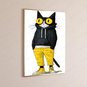 K&ouml;nnte beinhalten: Ein gerahmter Wandkunstdruck, der eine schwarz-wei&szlig;e Katze mit gro&szlig;en gelben Augen zeigt. Die Katze tr&auml;gt einen schwarzen Kapuzenpullover mit wei&szlig;en Kordeln, eine leuchtend gelbe Hose und passende gelbe High-Top-Sneaker und steht auf einem gr&uuml;nen Fleck.