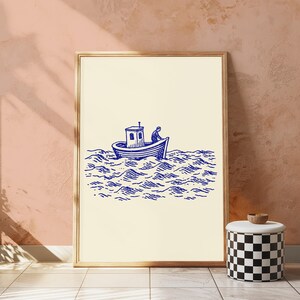 May include: A framed wall art print featuring a blue ink illustration on a cream background. The artwork depicts a small boat with a cabin and a single figure on board, navigating through stylised, wavy ocean water lines.