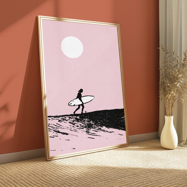 K&ouml;nnte beinhalten: Ein gerahmter vertikaler Wandkunstdruck mit einer minimalistischen Illustration einer Silhouette, die ein Surfbrett &uuml;ber eine texturierte schwarze Landschaft tr&auml;gt, vor einem hellrosa Hintergrund mit einer gro&szlig;en wei&szlig;en Sonne.
