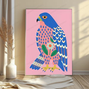 May include: A rectangular wall art print featuring a stylized blue falcon against a solid pink background. The bird has a yellow beak, orange eye, and patterned feathers with a central white flower graphic. The bird stands on yellow talons.