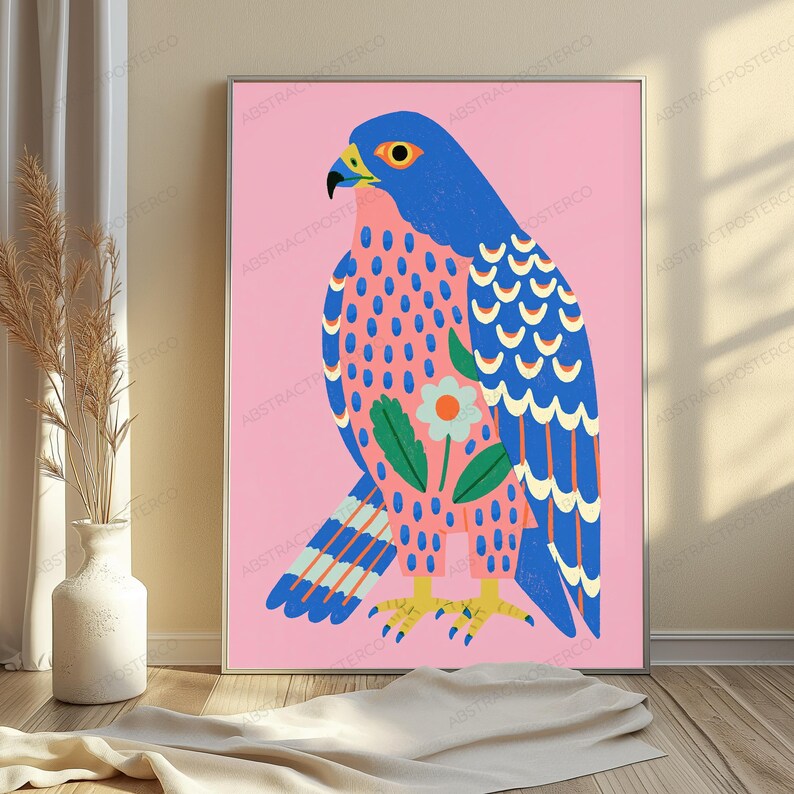 May include: A rectangular wall art print featuring a stylized blue falcon against a solid pink background. The bird has a yellow beak, orange eye, and patterned feathers with a central white flower graphic. The bird stands on yellow talons.