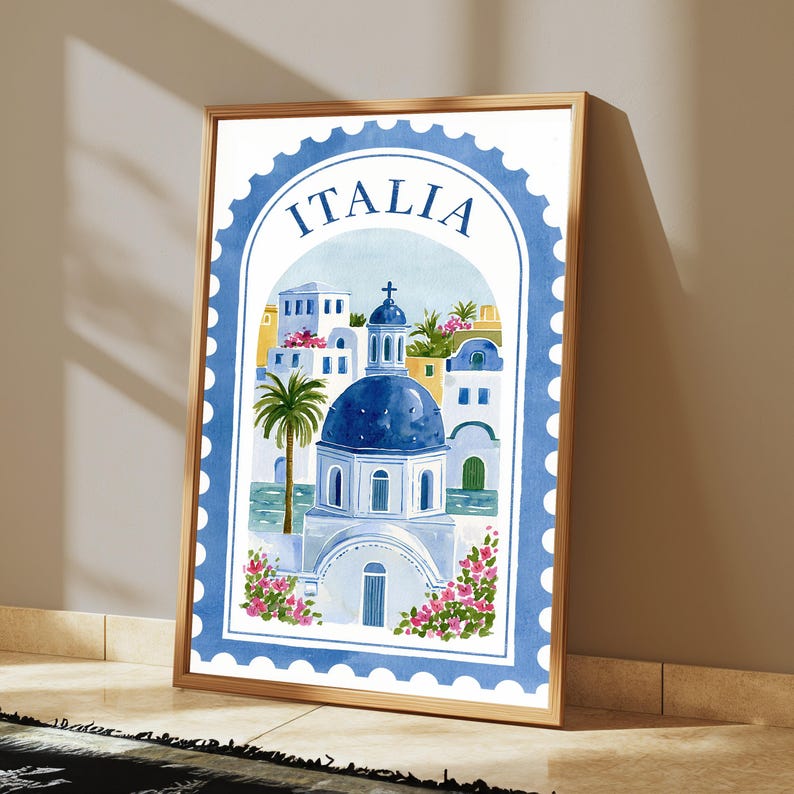 May include: A framed wall art print featuring a watercolor illustration of a Mediterranean coastal town with a blue domed church, palm trees, and pink flowers. The design is shaped like a postage stamp with a blue border and the text ITALIA.
