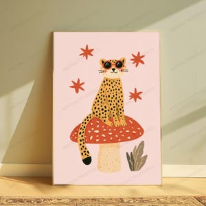 Op de afbeelding: Een ingelijste kunstprint op een lichtroze achtergrond met een gevlekte luipaard die een ronde oranje zonnebril draagt, zittend op een grote rode paddenstoel met witte stippen, omringd door vier oranje sterren en een kleine grijze plant.