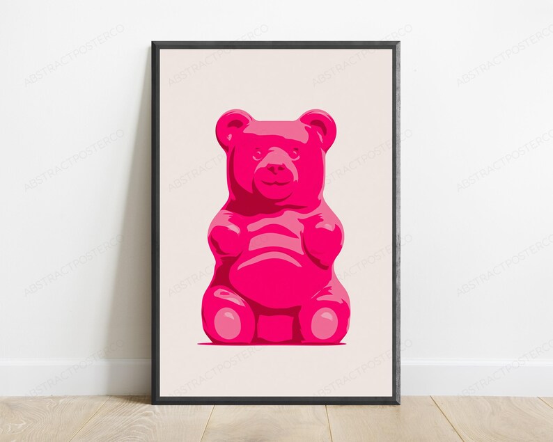 May include: A framed wall art print featuring a centered, stylized illustration of a bright pink gummy bear. The bear is depicted with a smooth, glossy appearance against a solid, light beige background, enclosed within a thin black frame.
