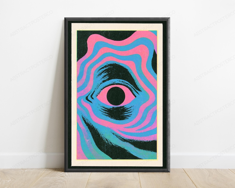 May include: A framed rectangular wall art print featuring a central black pupil surrounded by a pink iris. The eye is set against a background of wavy, concentric bands of alternating bright pink and cyan blue, with dark textured brushstroke accents.