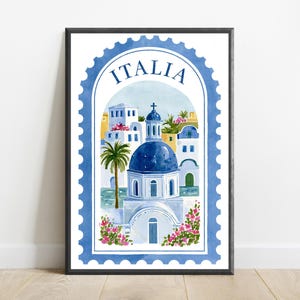 May include: A framed wall art print featuring a watercolor illustration of a Mediterranean coastal scene shaped like a postage stamp. The design includes a blue domed building, white architecture, palm trees, and pink flowers with the text ITALIA.