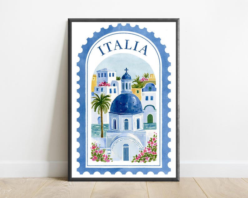 May include: A framed wall art print featuring a watercolor illustration of a Mediterranean coastal scene shaped like a postage stamp. The design includes a blue domed building, white architecture, palm trees, and pink flowers with the text ITALIA.