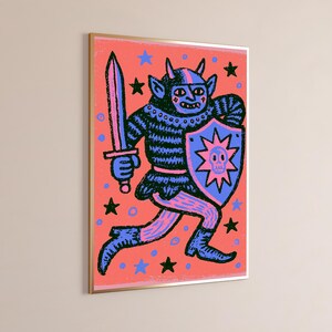 May include: A framed wall art print featuring a dark blue horned creature in a striped tunic holding a sword and a shield with a skull emblem. The background is a vibrant coral color decorated with small blue and black stars and circular dots.