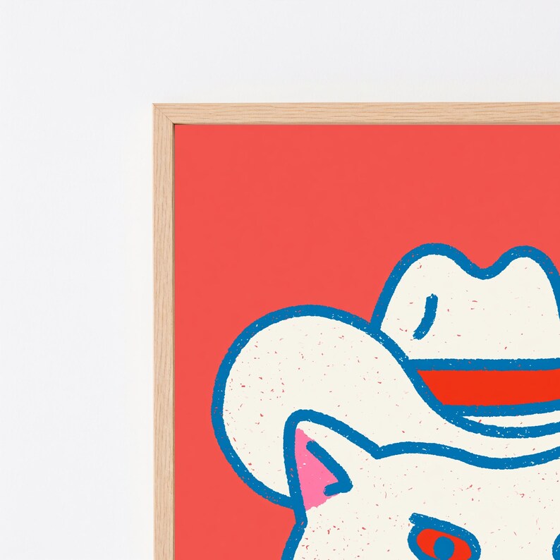 May include: A framed wall art print featuring a stylized white cat wearing a white cowboy hat with a red band. The cat has pink inner ears and red eyes, set against a vibrant red background. The illustration uses a textured, graphic art style.
