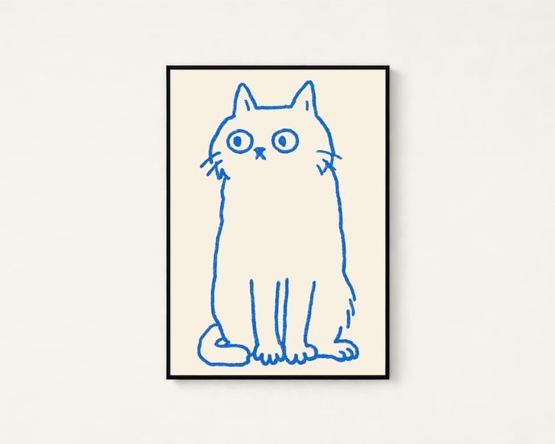 May include: A framed wall art print featuring a simple, hand-drawn illustration of a cat in bright blue ink on a cream-colored background. The cat is depicted in a seated position with wide, circular eyes and a small, minimalist facial expression.