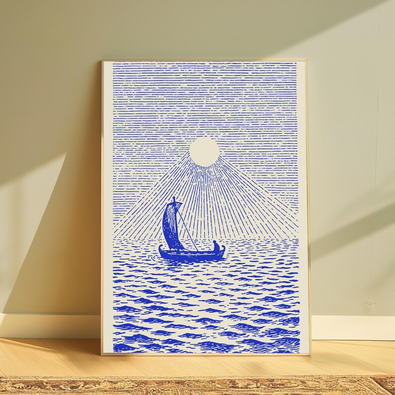 May include: A rectangular wall art print featuring a blue ink illustration on a cream background. The artwork depicts a small sailboat with a single sail on a textured sea, beneath a large circular sun with radiating lines extending outward.