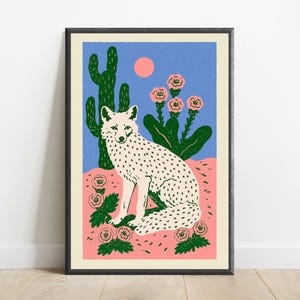 Pu&ograve; includere: Una stampa artistica incorniciata raffigurante una volpe bianca con macchie nere seduta in un paesaggio desertico. La scena include un alto cactus verde, fiori rosa, un cielo azzurro e un sole rosa pallido, in uno stile grafico piatto.