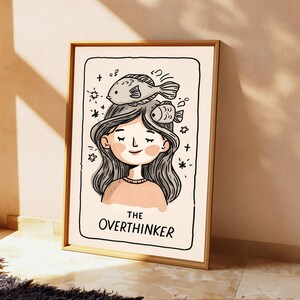 K&ouml;nnte beinhalten: Ein gerahmter Kunstdruck mit einer schwarz-wei&szlig;en Strichzeichnung einer Person mit langem Haar und zwei Fischen auf dem Kopf. Der Text THE OVERTHINKER ist unten aufgedruckt. Die Illustration verwendet einen cremefarbenen Hintergrund mit zartrosa Akzenten.