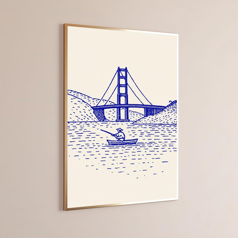 May include: A framed wall art print featuring a blue line drawing on a cream background. The illustration depicts a suspension bridge spanning across water with a small boat and a person fishing in the foreground, rendered in a simple sketch style.