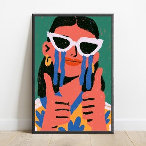 May include: A framed art print featuring a stylized illustration of a person with dark hair wearing white cat-eye sunglasses. The person has blue tears streaming down their face, is giving a double thumbs-up, and wears a yellow and blue patterned shirt.