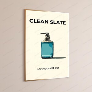 May include: A rectangular wall art print featuring a cream-colored background with the black text CLEAN SLATE at the top and sort yourself out at the bottom. Centered is a hand-drawn illustration of a blue liquid soap dispenser with a pump.