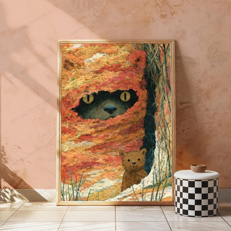 May include: A rectangular framed wall art print featuring a textured, orange and yellow knitted hood covering a dark creature with bright yellow eyes. Below the hood, a small, brown, furry creature stands near a dark, vertical opening.