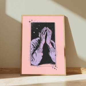 May include: A framed art print featuring a light purple illustration of a person with their hands covering their face. The figure is set against a black rectangular background filled with white stars, all centered on a solid light pink field.