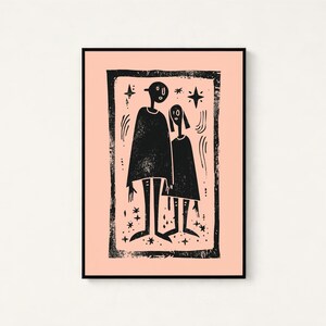 May include: A framed wall art print featuring a black ink block print illustration of two stylized figures standing together on a light peach background. The artwork is enclosed in a thick, textured black border with small star and line accents.