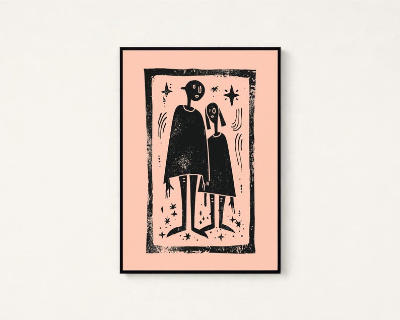 May include: A framed wall art print featuring a black ink block print illustration of two stylized figures standing together on a light peach background. The artwork is enclosed in a thick, textured black border with small star and line accents.