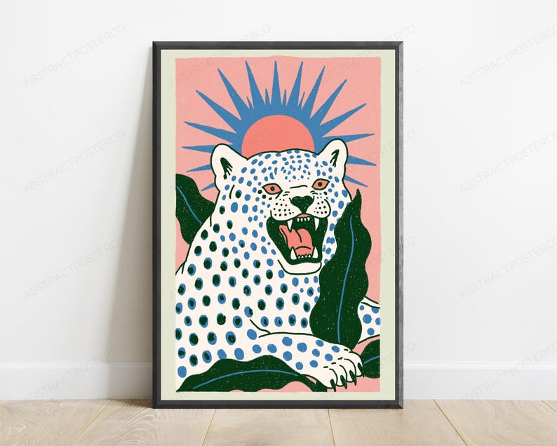 May include: A framed art print featuring a white leopard with blue spots and an open mouth, set against a pink background with a blue sunburst graphic. The leopard is surrounded by dark green tropical leaves, all enclosed in a black frame.