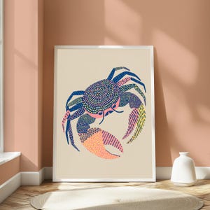 May include: A framed wall art print featuring a stylized crab illustration on a light beige background. The crab is rendered in dark blue, pink, and yellow, with intricate patterns of dots and lines covering its shell and large pincers.