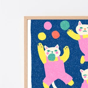 K&ouml;nnte beinhalten: Ein gerahmter Kunstdruck mit wei&szlig;en Katzen mit gelben Armen, die rosa Latzhosen tragen, vor einem dunkelblauen, texturierten Hintergrund. Die Katzen jonglieren mit bunten Kugeln in den Farben Rosa, Gr&uuml;n, Gelb und Orange mit k&ouml;rniger Textur.