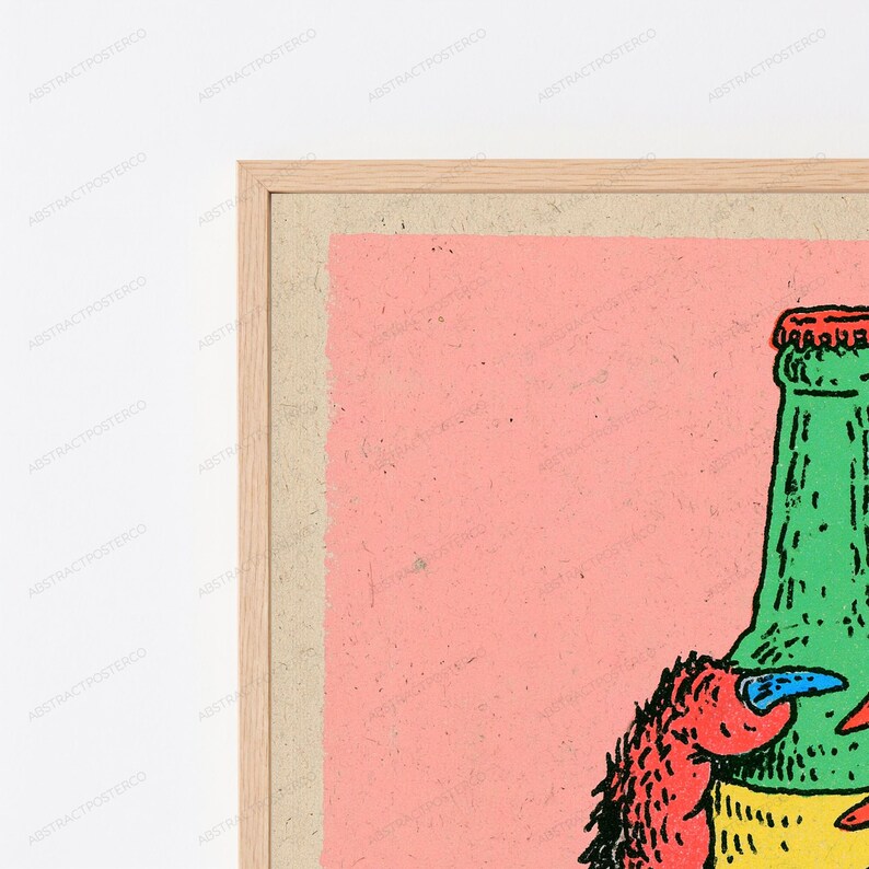 May include: A framed art print featuring a graphic illustration of a green bottle with a red cap and a red creature with a blue claw. The artwork is set against a solid light pink background, enclosed within a light-toned wooden frame.